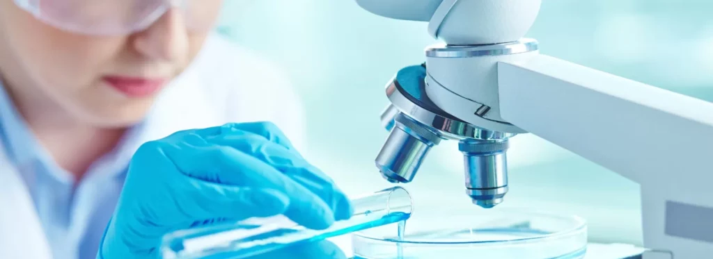 Lab technician in a white coat examining a sample under a microscope and handling phages in a Petri dish.