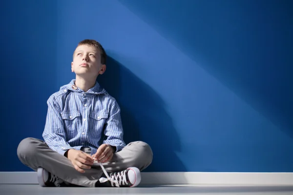 Jeune enfant autiste en contemplation, assis contre un mur bleu, illustrant la réflexion intérieure et les recherches en phagothérapie.